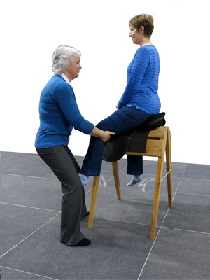 Pupil is shown on a saddle with teacher manipulating left leg
